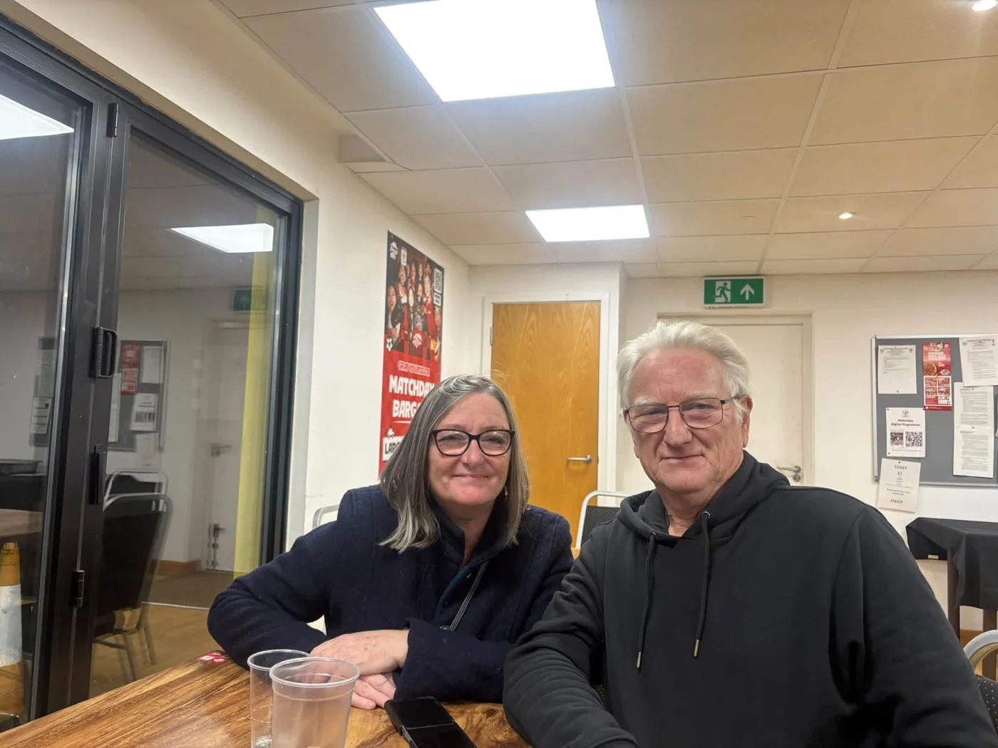 A woman and a man sit at a table in the clubhouse at East Grinstead Town FC