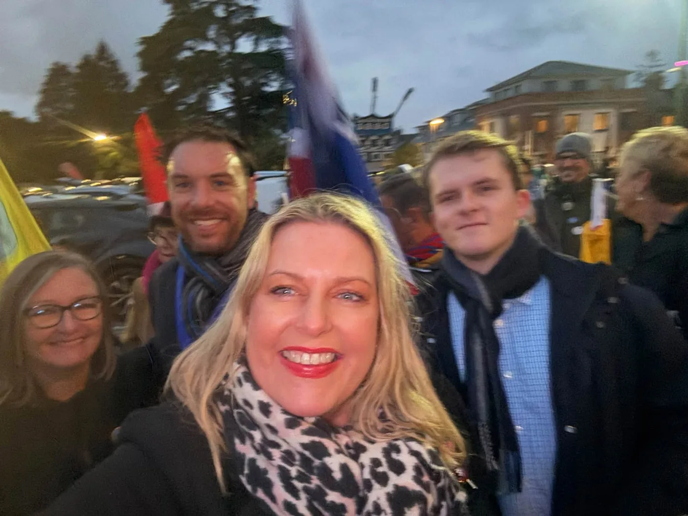 Mims Davies MP takes a selfie at dusk with Cllr Ed Godwin, Cllr Jacquie Russell and others in a crowd, flags behind them
